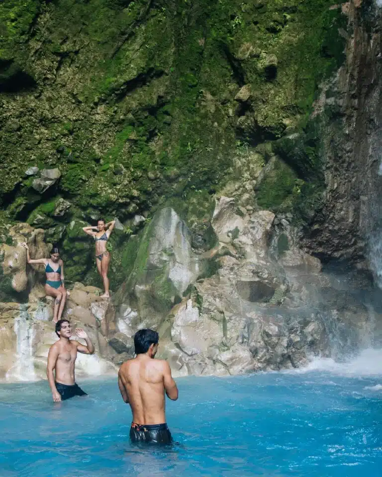Guests in a turquoise mineral pool beneath the waterfall at Sensoria