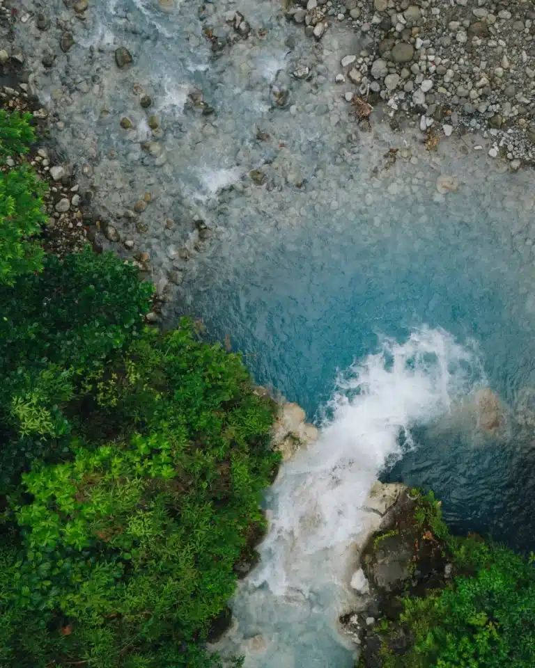 Aerial view of a waterfall pouring into a turquoise river at Sensoria