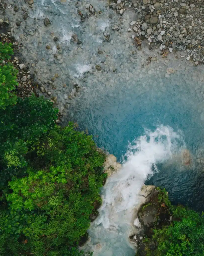 Aerial view of a waterfall pouring into a turquoise river at Sensoria