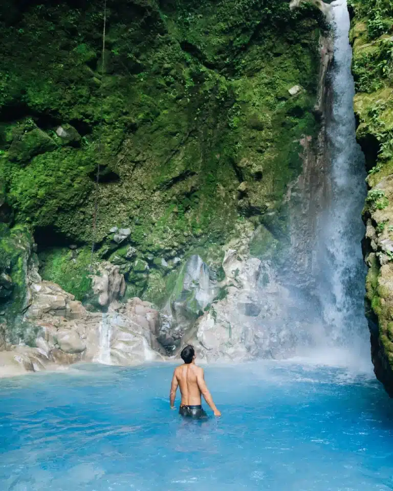 Guest beneath a waterfall in a turquoise pool at Sensoria
