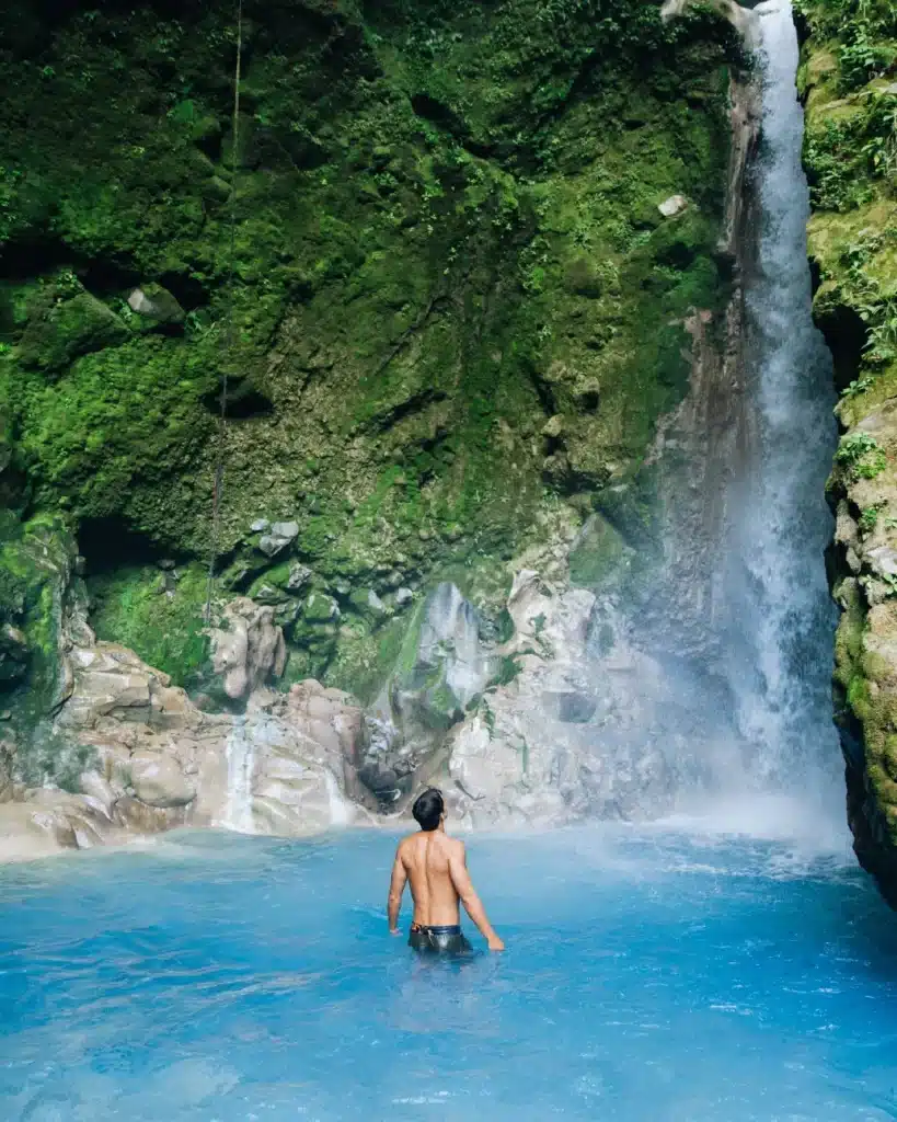 Guest beneath a waterfall in a turquoise pool at Sensoria